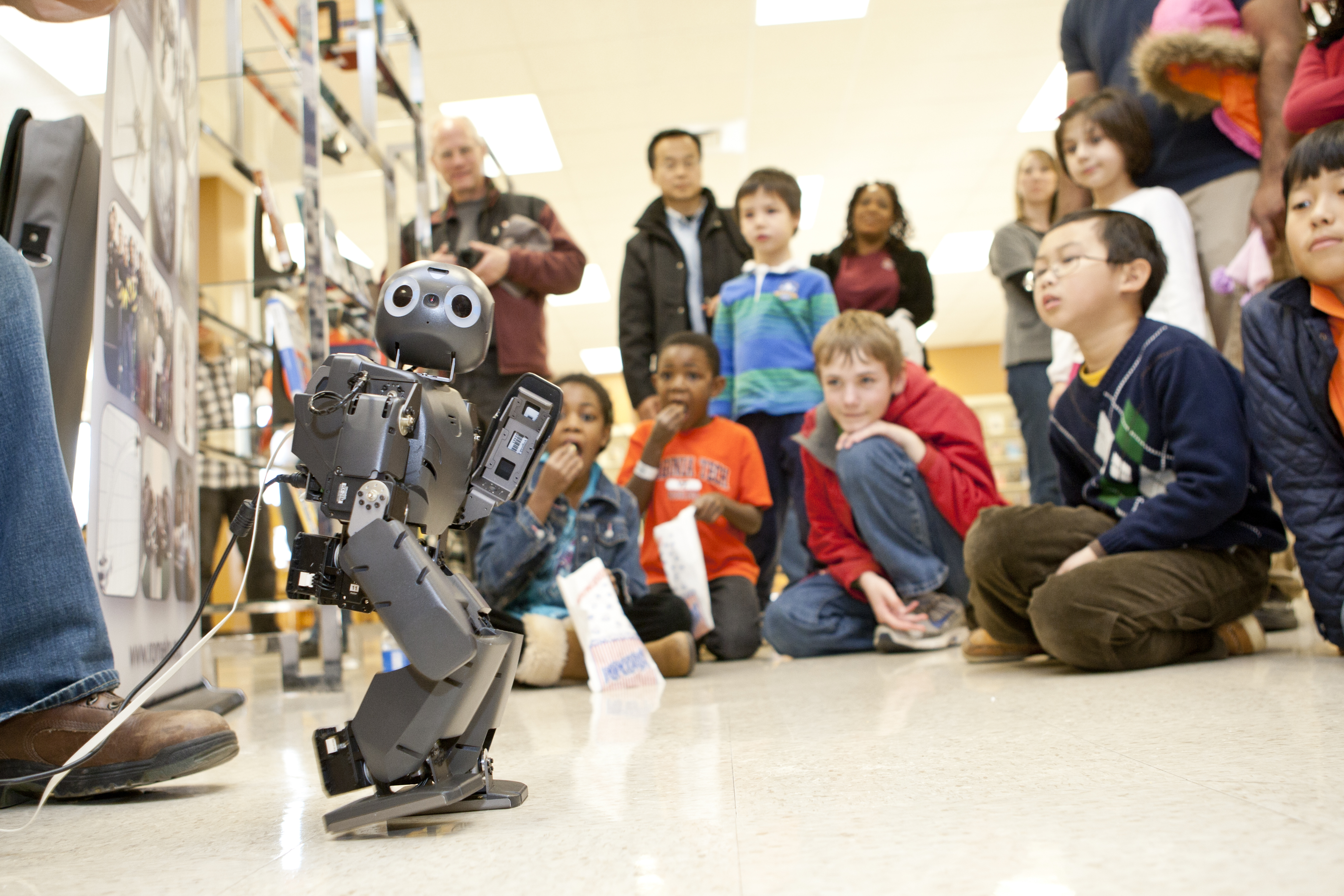 Children watch DARwIn, one of Virginia Tech's robots, play with a ball during an event.