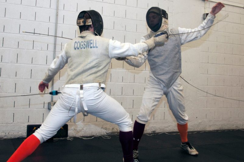 Two students fence while dressed in fencing attire
