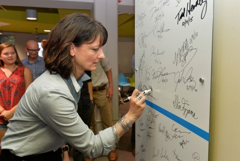 Regina Dugan signs the whiteboard with other entrepreneur signatures, as Innovate students look on.
