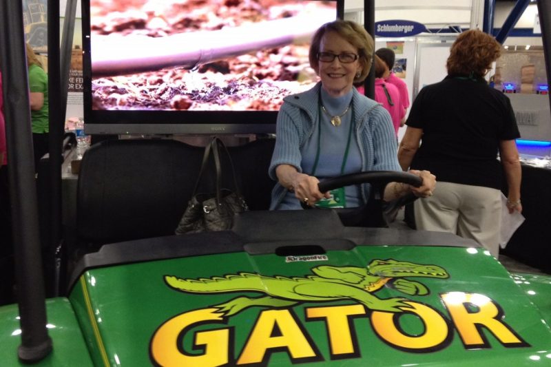In the photo, Mary smiles while posing in the driver's seat of a green Gator cart.