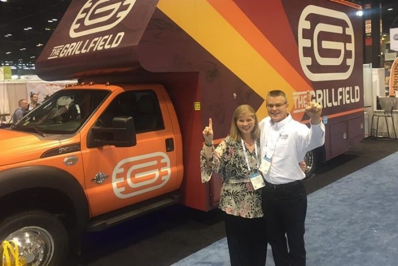 Patty Perillo and Ted Faulkner pose with The Grillfield in the background at the conference. 