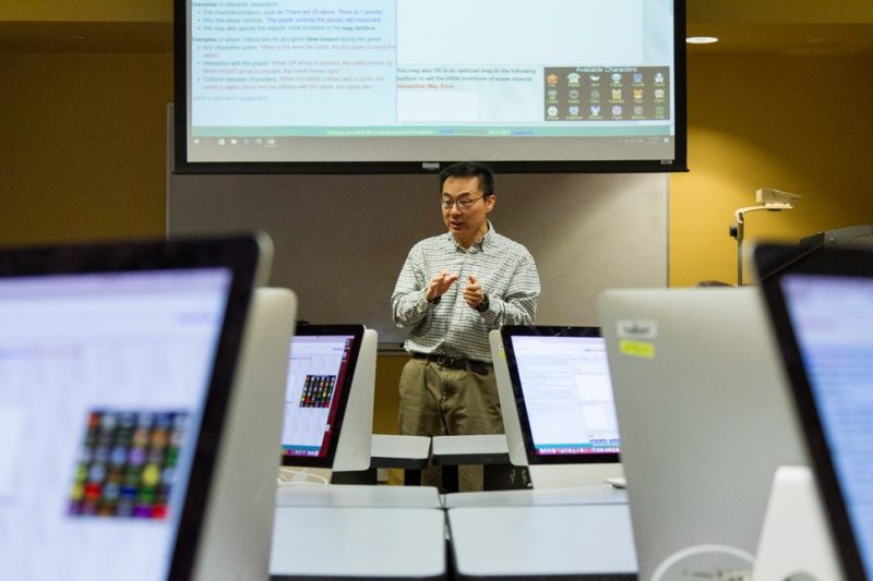 Photo of Michael S. Hsiao standing in the center of a classroom filled with Macs with GameChangineers on the screens.