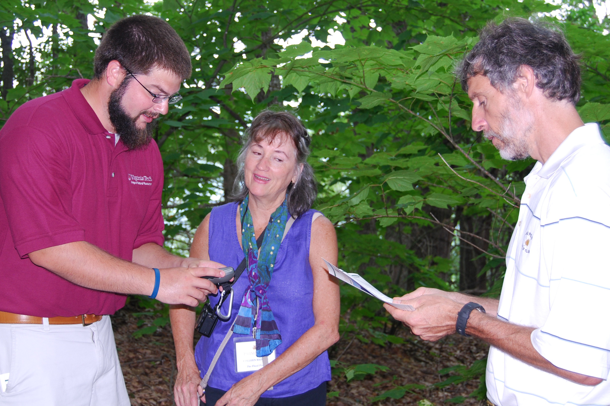 An instructor showing two participants how to use a GPS in a wooded setting.