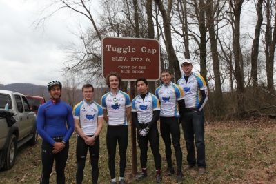 Group of bicyclists stand before an elevation marker.