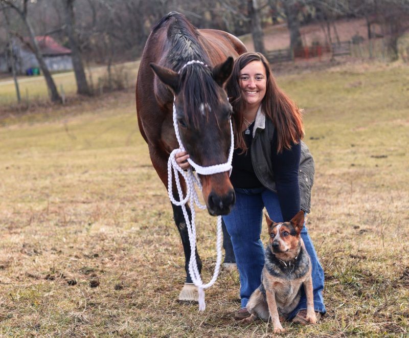 Morgan Sowers standing with a dog and horse in a field.