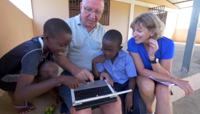 Man sits flanked by two young Haitians and a woman looking at a laptop computer.