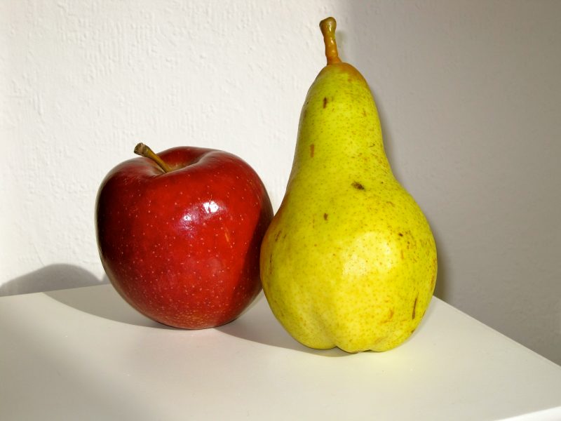 An apple and a pear sit next to each other on a table.