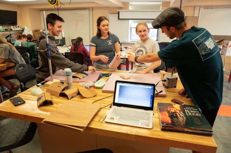 Four students stand around a large table in a makerspace, working together on a project.