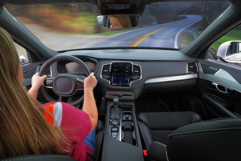 A woman drives down the road. She is holding both hands on the wheel and her eyes are facing forward. Integrated hands-free devices are built into the car and allow drivers to talk on the phone and use GPS without removing their hands from the wheel or eyes from the roadway.
