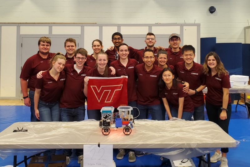 2019 Chem-E-Car Team poses for a photo. Their small car sits on a table in front of them.