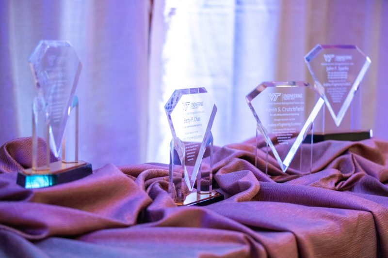 Four glass awards sit on a table covered by decorative tablecloths.