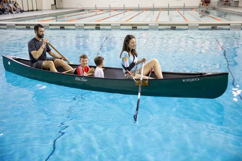 With one arm, a woman and her family paddle a canoe around the pool at War Memorial Hall
