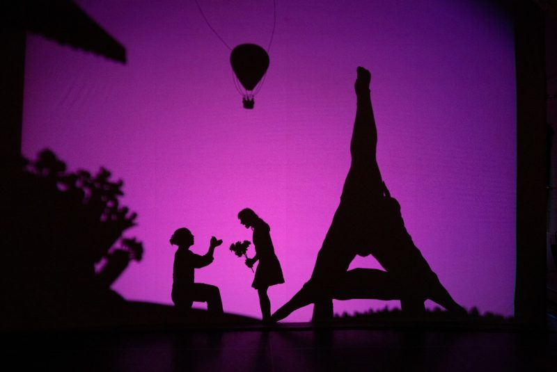 A silhouette of a man proposing to a woman under an hot air balloon.