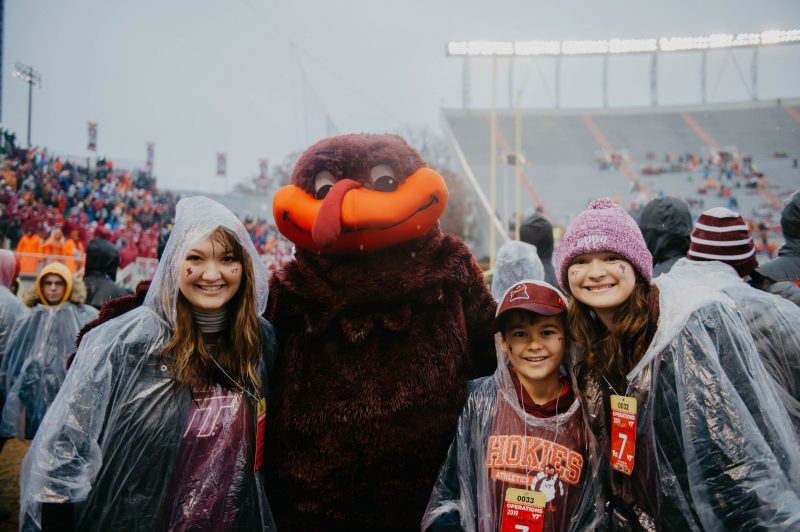 Sammie Dailly, the Hokie Bird, and Dailly's younger brother and sister, pose in the rain for a photo in Lane Stadium.