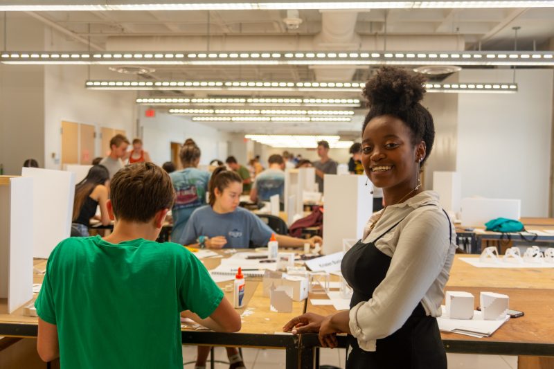 Aria Hill, who attended the Inside Architecture + Design camp during the summer of 2016 as a high school student, poses in front of students participating in the workshop..