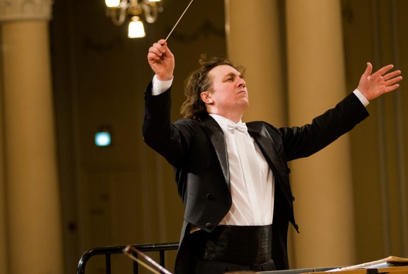 Volodymyr Sirenko, conductor for the National Symphony Orchestra of Ukraine, stands onstage is a tuxedo, baton raised in the air, leading the orchestra.