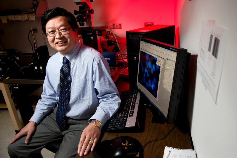 Portrait of XJ Meng in a lab next to  computer