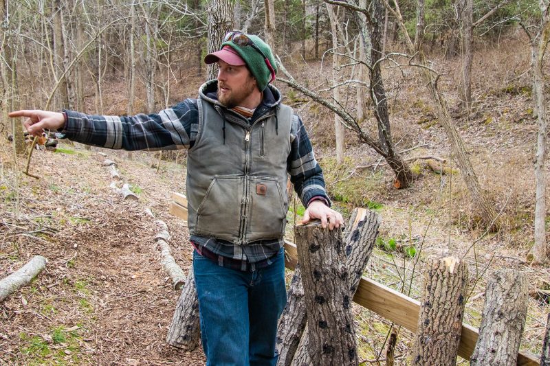 Adam Taylor points while standing next to several logs used to grow mushrooms.