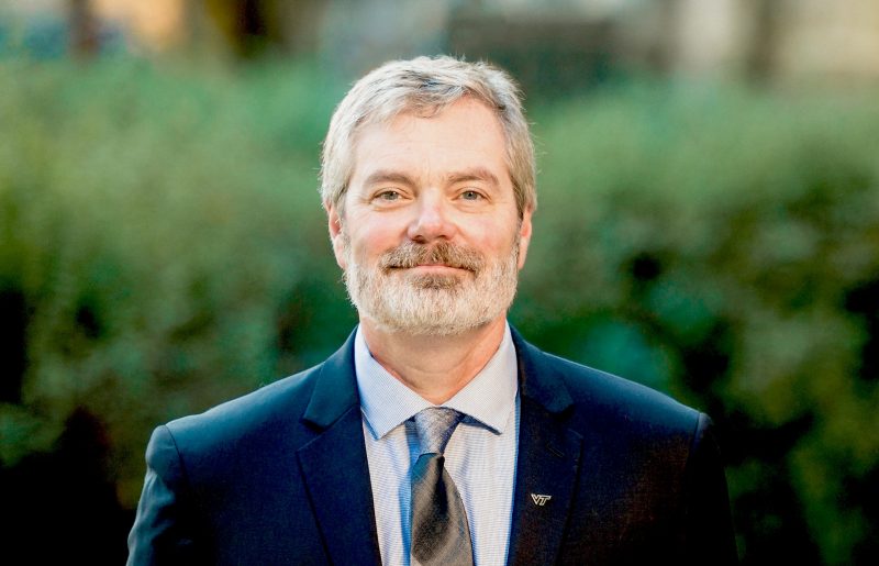 Steve Holbrook, professor and head of the Department of Geosciences, poses in a suit and tie, with a "VT" pin on his lapel.