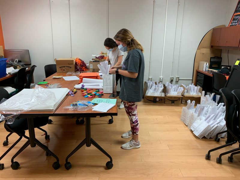 Two girls seen wearing masks and creating crafts for virtual homecoming decorations. 