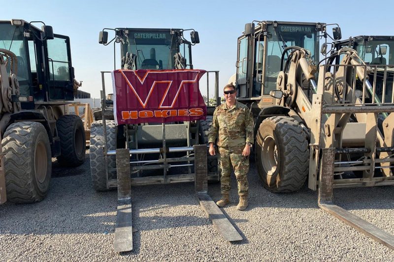 Maj. Michael Biederman stands in front of a row of heavy equipment and next to a Virginia Tech flag.