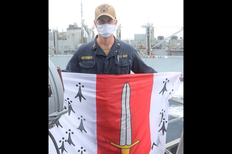 U.S. Navy Ensign Jake McCormick holds a Corps of Cadets flag while standing onboard the USS Cole.