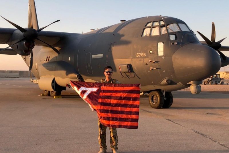 U.S. Air Force Capt. Jordan Schafer holds a Virginia Tech flag in front of an HC-130J, a fixed-wing search-and-rescue aircraft.