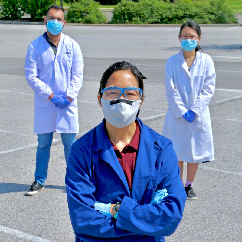 Photo of three scientists standing in masks and gloves.