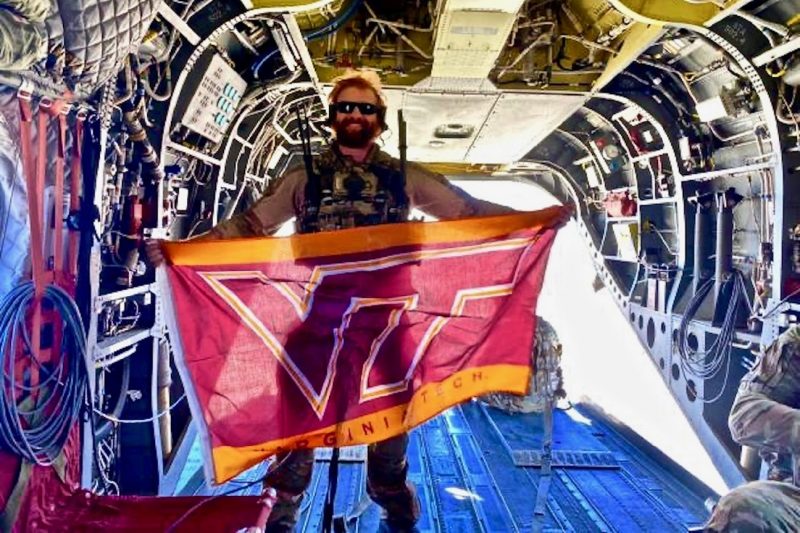 U.S. Air Force Capt. Garrett Treaster holds a Virginia Tech flag while standing in an aircraft.