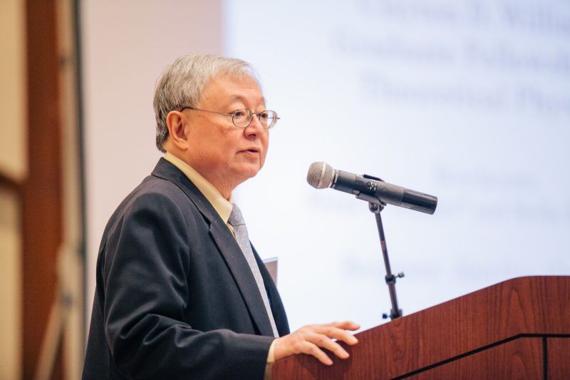 Lay Name Chang speaking at the podium at a college awards ceremony in 2017. He is wearing a dark suit and yellow dress shirt.
