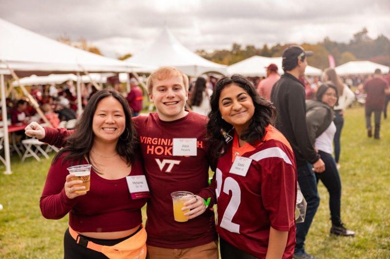 Young alumni posing and smiling at a tailgate. 